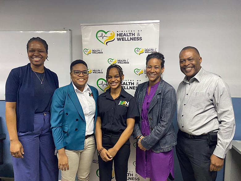 Jamaica team standing in front of the Ministry of Health and Wellness banner