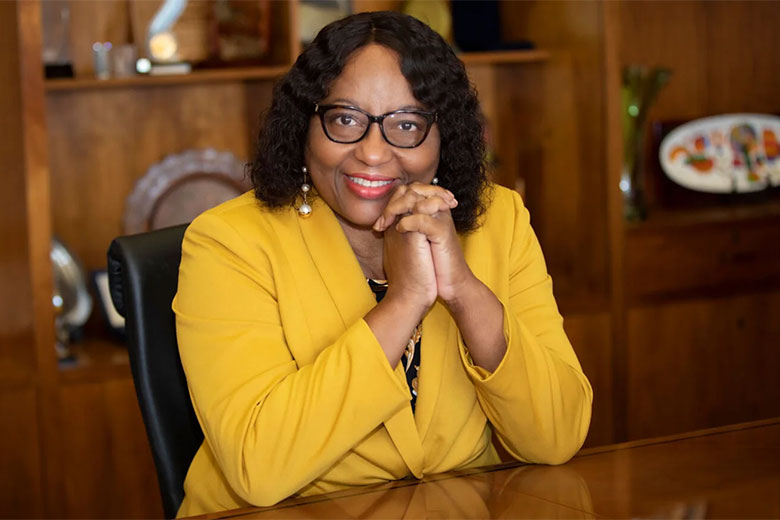 Dr. Carissa F. Etienne sitting at a desk wearing a yellow jacket