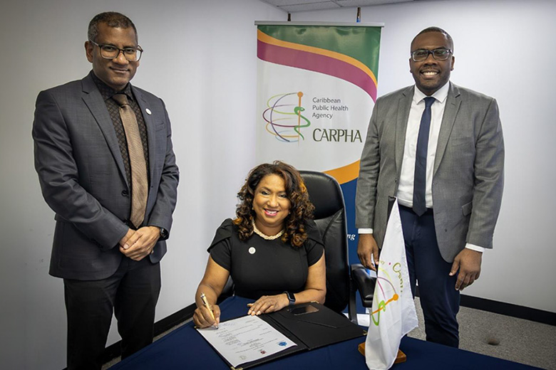 3 people 2 men standing and a woman sitting at a desk signing a document