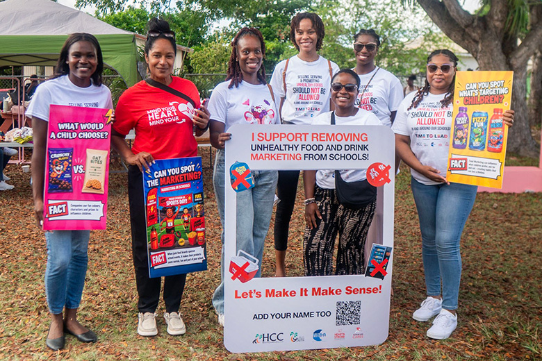 Campaigners hold colourful posters and a large sign stating "I support removing unhealthy food and drink marketing from schools!"