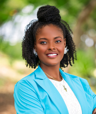 Smiling Black woman with natural curls in a top bun, wearing a bright blue blazer, white lace top, and gold cross necklace, outdoors