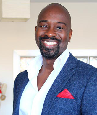 Portrait of a smiling man wearing a textured blue jacket, white open-neck shirt, and vibrant red pocket square in a light room