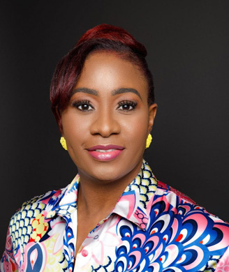 Smiling Black woman with styled reddish-burgundy hair, yellow statement earrings, and a colourful patterned shirt against a dark background