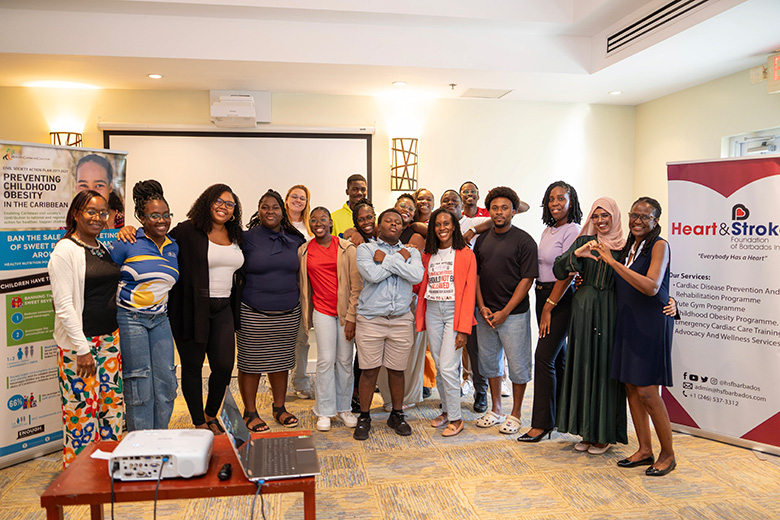 Diverse group of participants smiling together in a conference room, posing between Heart & Stroke Foundation and HCC banners during a workshop