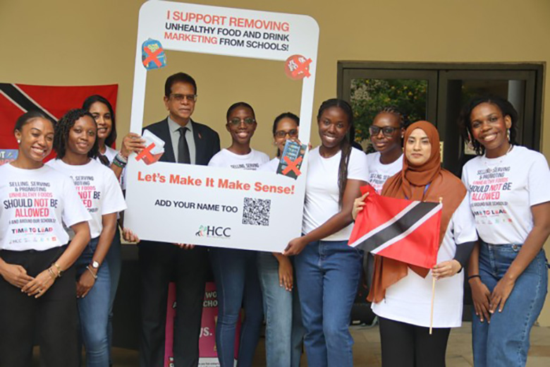 Group supporting removing unhealthy food and drink marketing from schools, holding campaign frame and Trinidad and Tobago flags