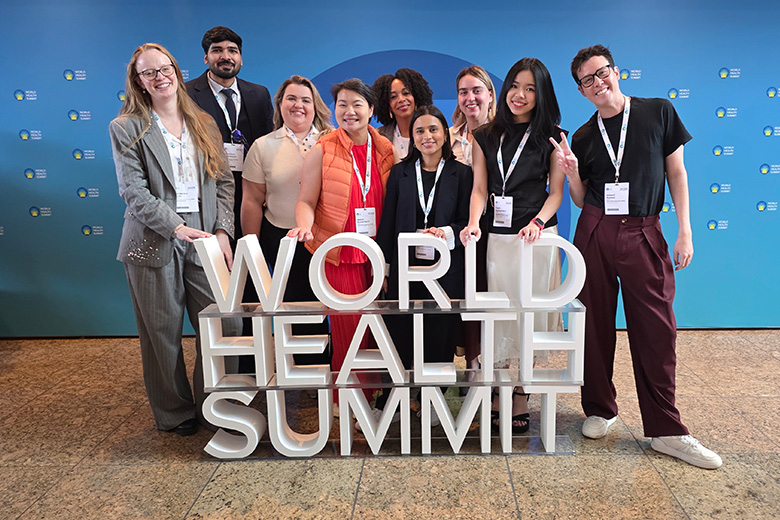 A group of young professionals pose in front of a blue World Health Summit wall around 3D letters spelling the event name