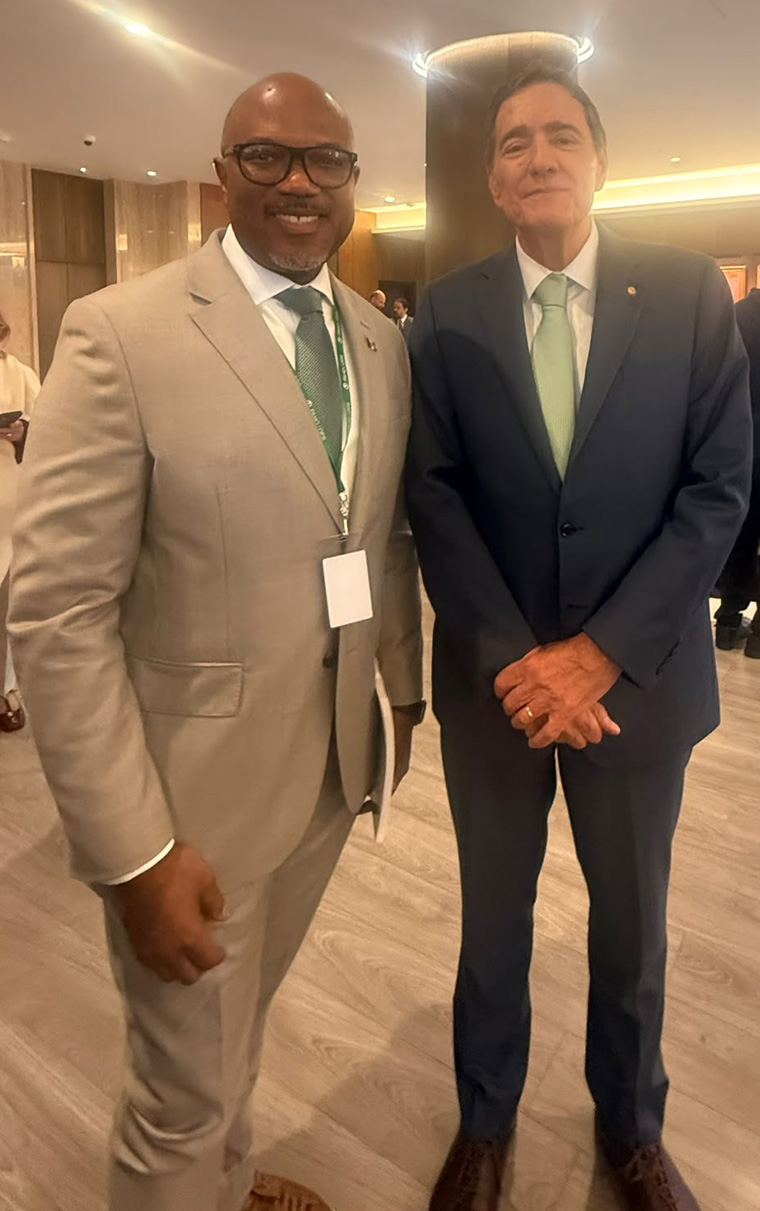 A man in a beige suit and glasses alongside a man in a dark navy suit and light green tie