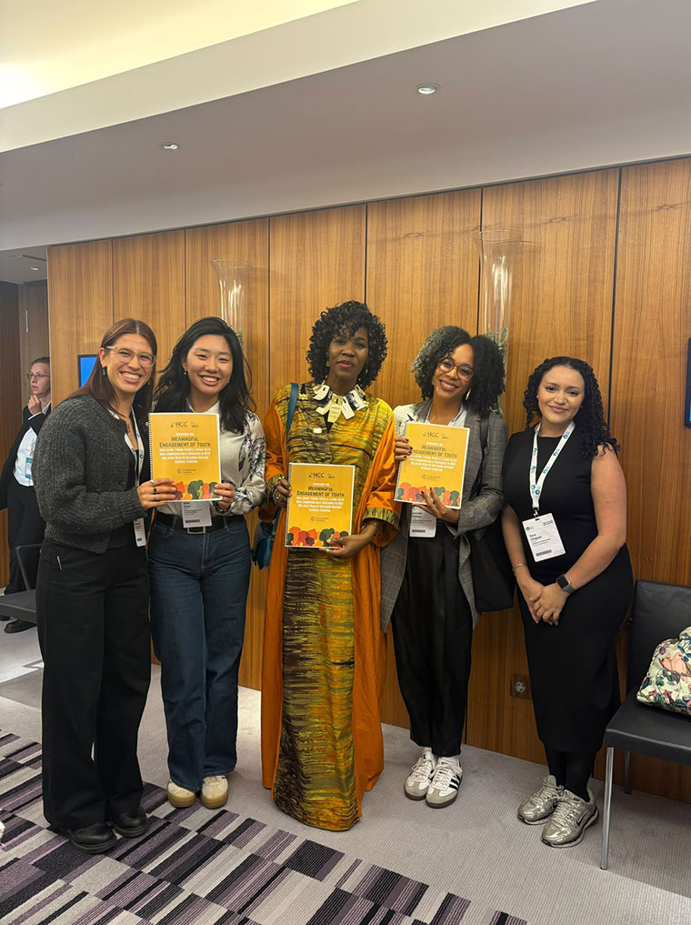 Five smiling women stand together indoors, three of them holding yellow HCC youth engagement report booklets